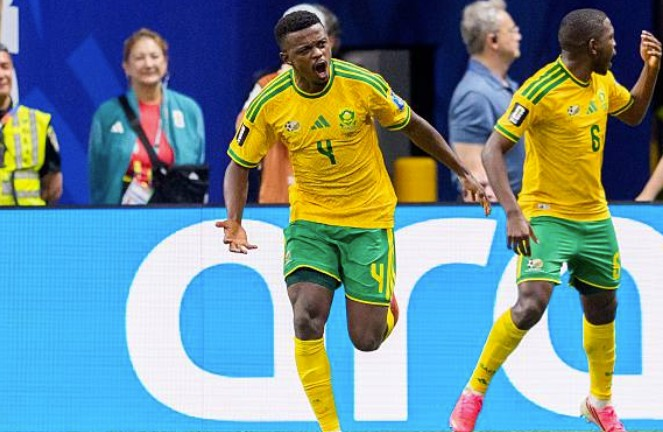Brazilian football players celebrate a goal on the field, shouting with arms outstretched near a blue advertising board behind them.