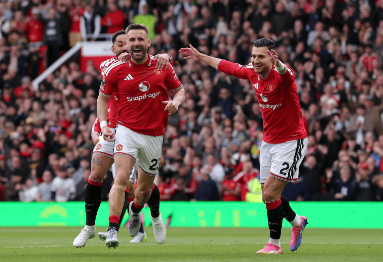 Manchester United players celebrate a goal on the pitch as the crowd cheers in the stands.