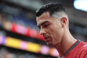 Close-up of a man with a high skin fade haircut wearing a red jersey, looking down.