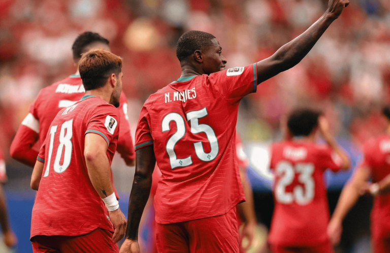 Soccer players in red jerseys celebrate on the field; the central player wearing number 25 raises his arm in celebration.