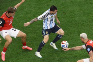 Soccer players compete for the ball during a match on a green pitch, Argentine player in light blue white stripes controls the ball while two opponents close in.
