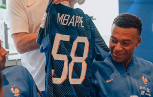 Blue sports jersey with the number 58 is held up, showing its back, as two people in blue team gear look on.