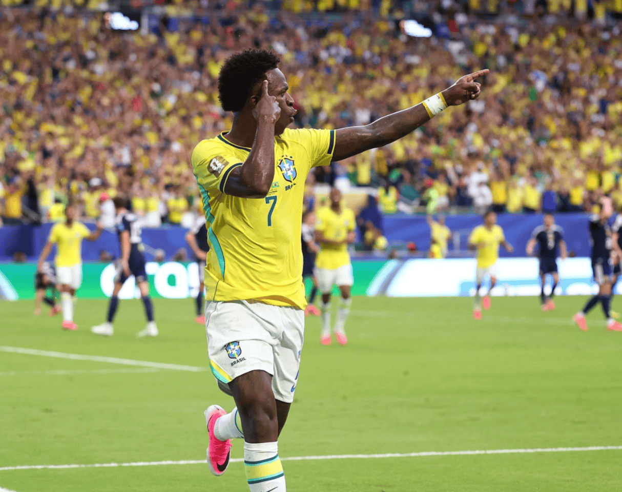 Brazilian soccer player in yellow kit (No. 7) celebrating a goal on the field with a large cheering crowd in the stands.