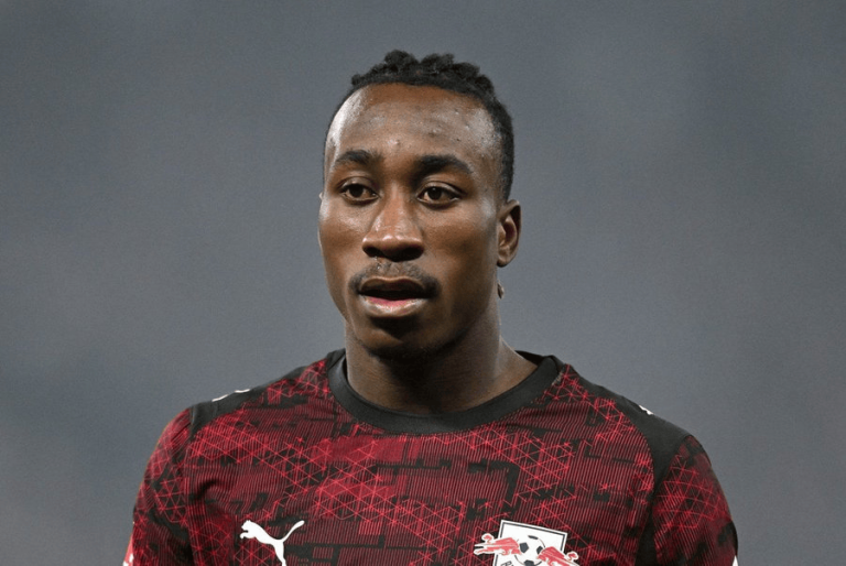 Portrait of a Black male footballer wearing a red and black Puma jersey with a Red Bull logo, facing forward with a neutral background.