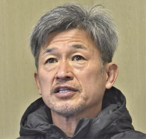 Asian man with gray hair and light stubble wearing a black puffer jacket, speaking in a neutral indoor setting?