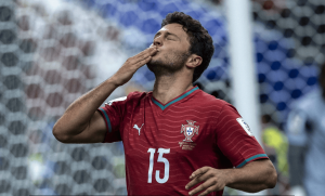 Portuguese footballer wearing number 15 jersey blowing a kiss" after a goal, on the pitch with a stadium background