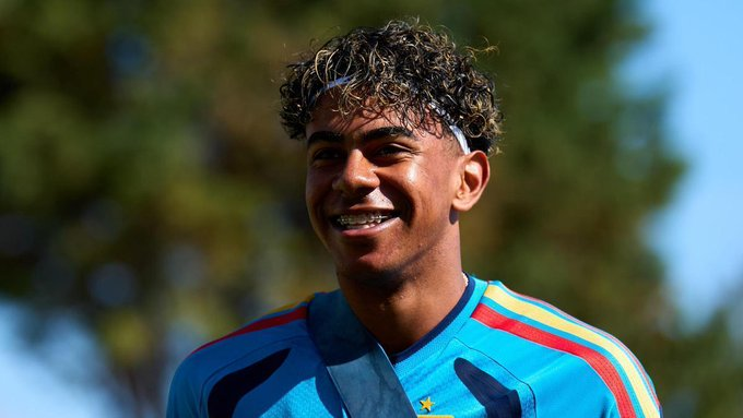 Smiling young man with braces, wearing a bright blue soccer jersey and a white headband, outdoors on a sunny day.