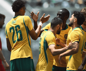 Soccer players in yellow and green uniforms celebrate with raised hands on the field after a play.