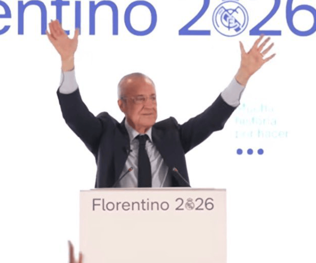 Older man in a suit at a podium with arms raised, campaign banner reading Florentino 2026 behind him.
