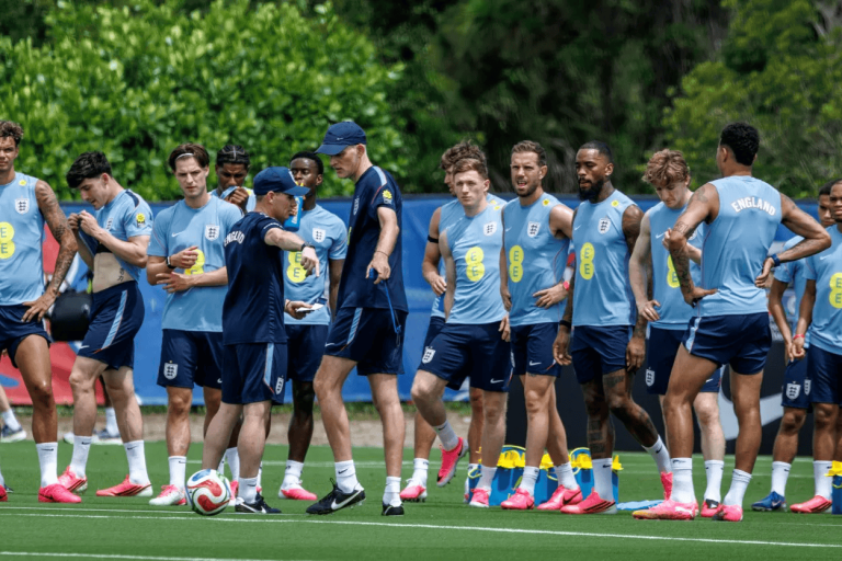 England men's football team in light blue training kits listening to coach during a drill on a grass field