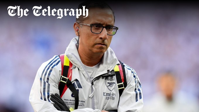 Man wearing an Arsenal-branded white jacket with harness straps, standing outdoors and looking serious; The Telegraph logo appears in the top-left corner.