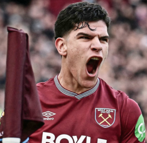 West Ham United player in maroon jersey shouting in celebration, mouth open, flag raised nearby.