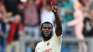Footballer in a cream AC Milan kit points upward with his right hand in celebration, blurred crowd in the background.