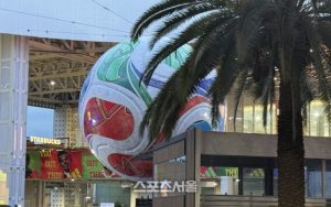 Large colorful sphere sculpture outside a modern building, with a palm tree and a Starbucks sign in view.