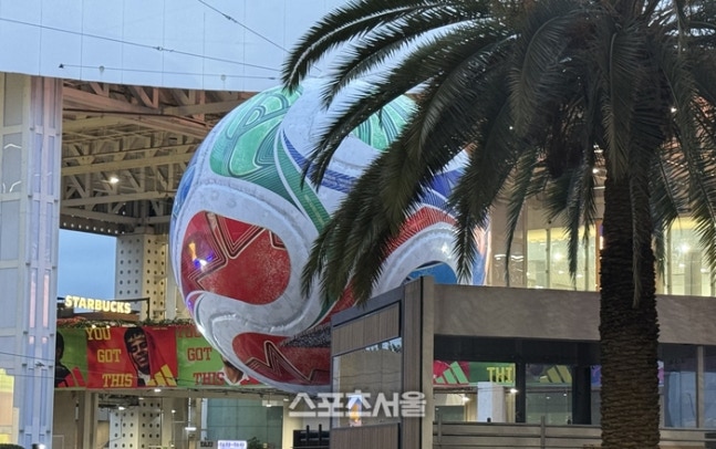 Large colorful sphere sculpture outside a modern building, with a palm tree and a Starbucks sign in view.