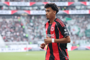 Soccer player in Eintracht Frankfurt jersey runs on the pitch with a blurred stadium crowd behind.
