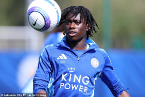 Footballer wearing a blue training kit heads a ball during practice on a sports field.