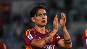Soccer player in maroon and orange Roma kit applauding on the field after a match.