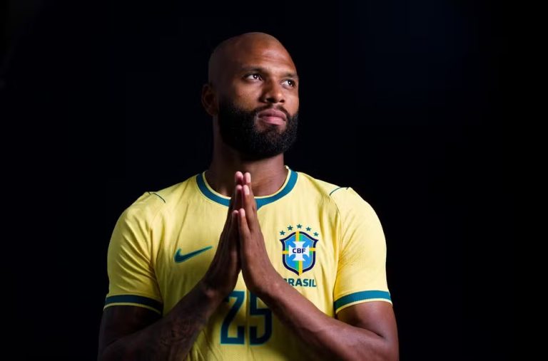 Male soccer player in Brazil national team jersey (#25) with hands pressed together in prayer, looking upward against a dark background.