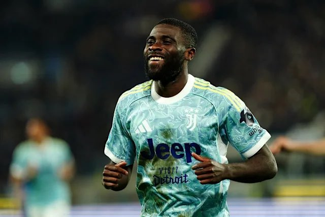 Soccer player in a light-teal Juventus away kit runs and smiles on the field during a match.