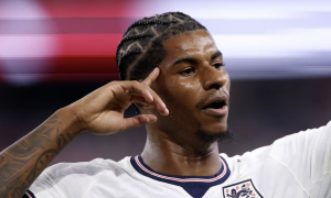 Close-up of a male footballer with braided hair and a tattooed arm, sweating, wearing an England jersey.