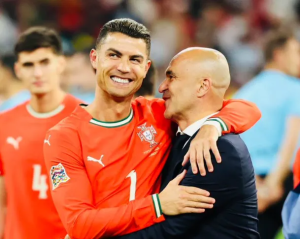 Portugal national team soccer player in a red jersey hugs a coach in a suit, both smiling on the field after a match.