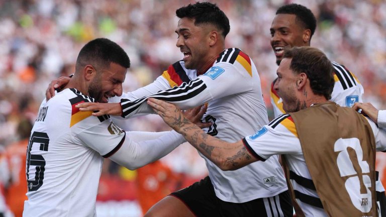 Soccer players in white jerseys celebrate together on the field, embracing and smiling during a match.
