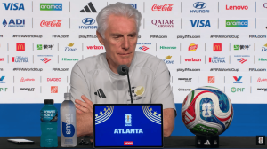 Male coach at a FIFA press conference with sponsor backdrop; tablet shows ATLANTA 2026 World Cup.