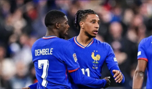 Two French national team football players in blue jerseys embrace on the field during a match, celebrating a moment of teamwork.