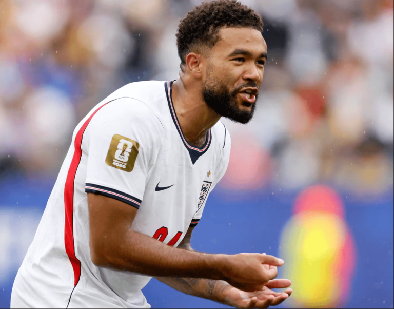 England footballer in a white kit with a World Cup patch on the sleeve, celebrating on the pitch.