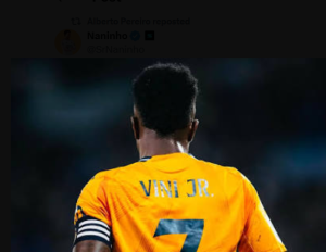 Back view of a footballer in an orange jersey with the name 'VINI JR.' and number 7 seen on the back, on a dim stadium field.