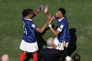 Two soccer players in blue jerseys celebrate with a high-five on a grassy field, a water bottle raised between them.