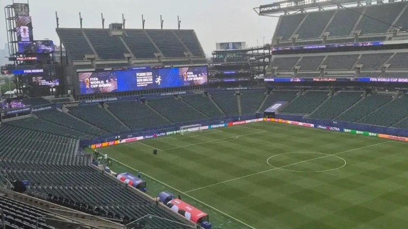 Empty football stadium with a green pitch and large video screens showing FIFA World Cup branding around the sidelines.