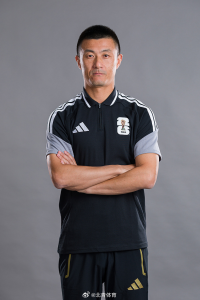 Asian man in a black FIFA polo with white stripes, arms crossed, posed against a gray studio background.