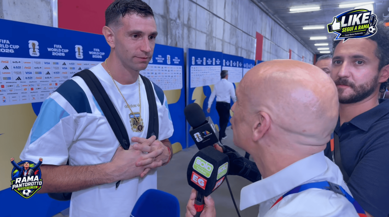 Athlete in a white shirt with backpack being interviewed by reporters holding microphones in front of a FIFA World Cup 2026 backdrop.