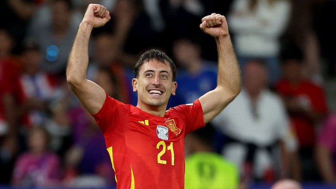 Soccer player in a red jersey with number 21 raises both arms in celebration on the field.