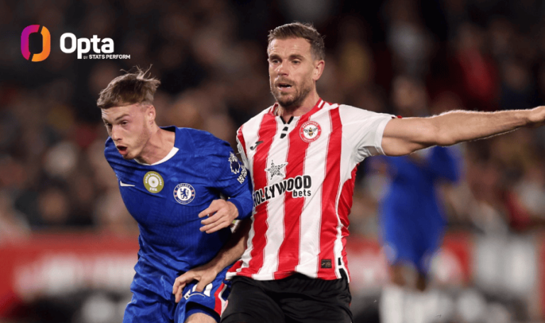 Two football players in blue and red-and-white kits compete for the ball on a crowded pitch, Opta logo top-left.