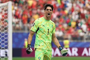 Soccer goalkeeper in a green jersey celebrating with a fist pump, standing by the goal as the crowd cheers behind him.