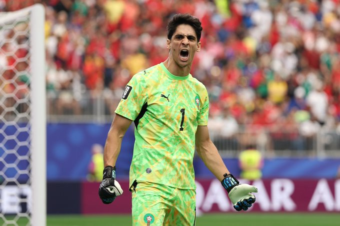 Soccer goalkeeper in a green jersey celebrating with a fist pump, standing by the goal as the crowd cheers behind him.