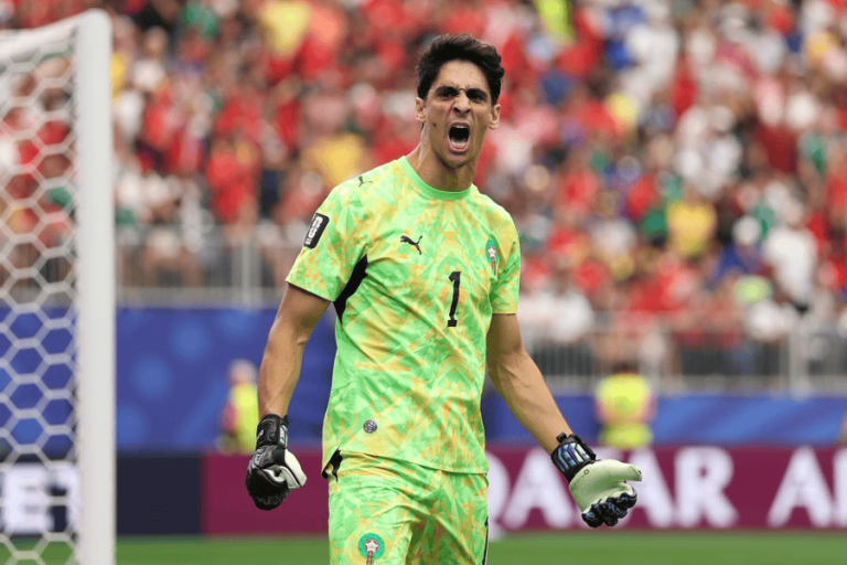 Soccer goalkeeper in a bright green kit (number 1) shouting on the pitch near the goal.