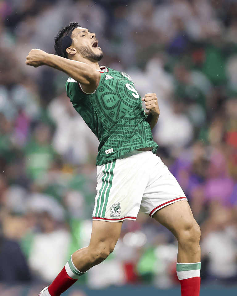 Soccer player in a green Mexico jersey celebrates a goal with a raised fist and open mouth.