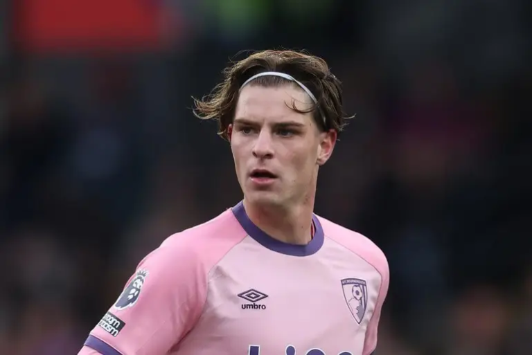Male soccer player in a pink kit with a white headband on a field, looking to the left with a focused expression.