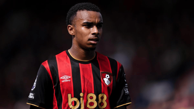 Male soccer player in a red and black striped jersey with a club crest, looking focused on the field.