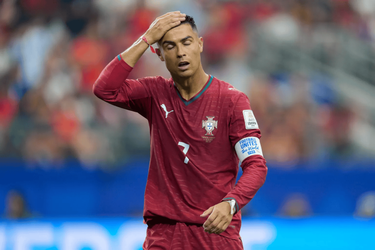 Portugal national team player in red kit with captain's armband, hand on forehead during a match on the field. This conveys fatigue or frustration in play.