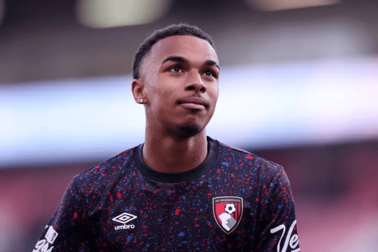 Young male footballer wearing a black speckled Bournemouth jersey, looking up, on a blurred stadium field.