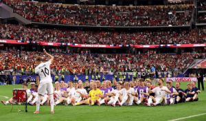 Soccer team posing for a group photo on the field as a packed stadium watches.