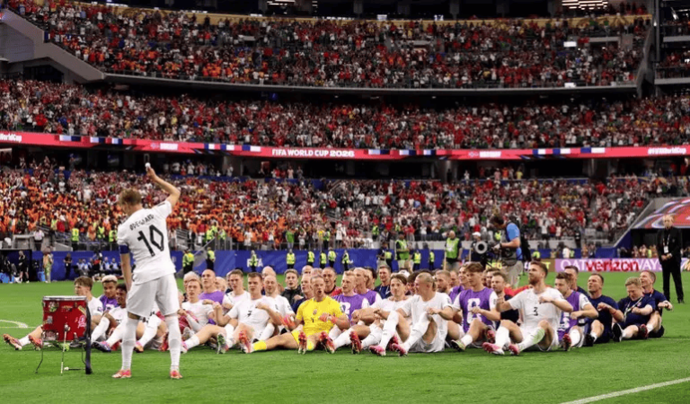 Soccer team posing for a group photo on the field as a packed stadium watches.