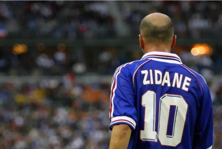 Back view of a soccer player in a blue jersey with 'ZIDANE' and the number 10, blurred stadium crowd in the background.