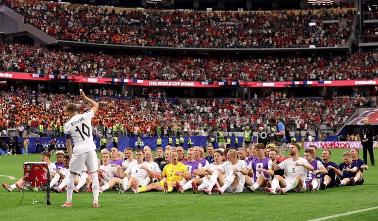 Soccer team posing for a group photo on the field as a packed stadium watches.