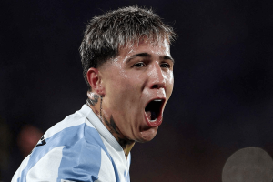 Soccer player in a light blue and white jersey shouting with mouth open on the field.